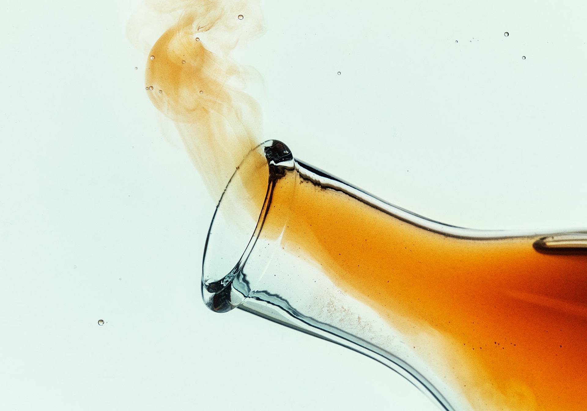 Close up image of orange fumes pouring out of the neck of a glass test tube bottle