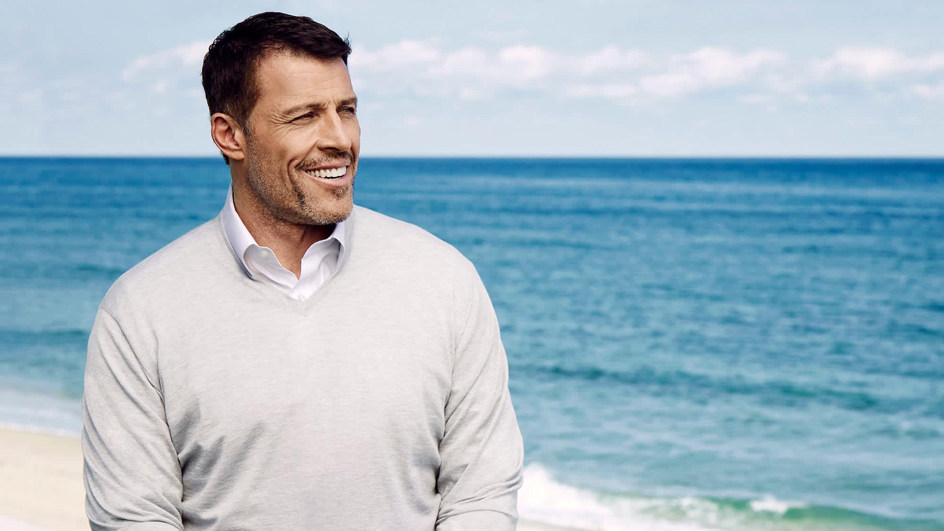 Tony Robbins landscape Photo head turned smiling in front of sea, to the left of the picture