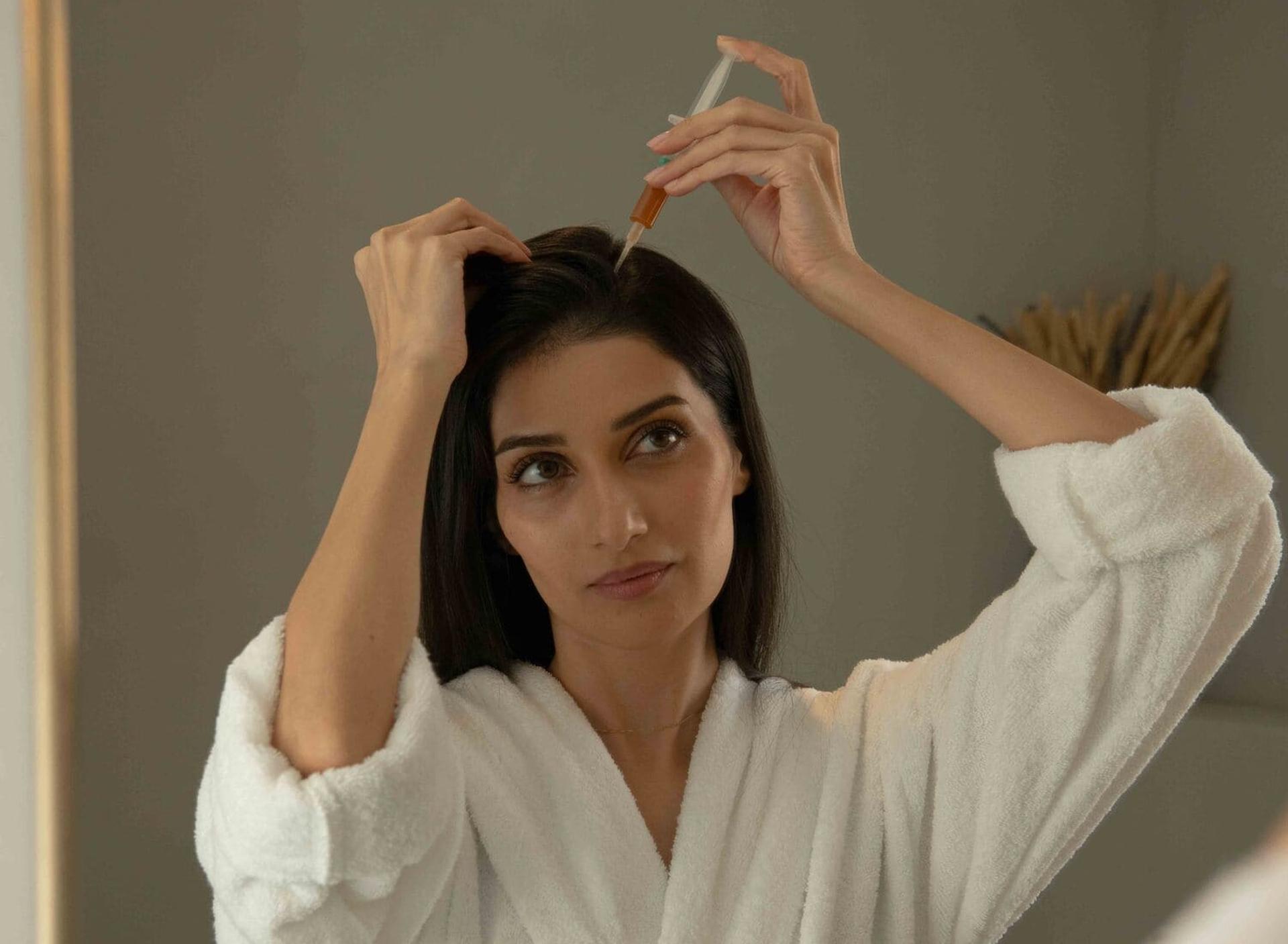Portrait photo of female with long dark hair applying Harklinikken hair gain extract