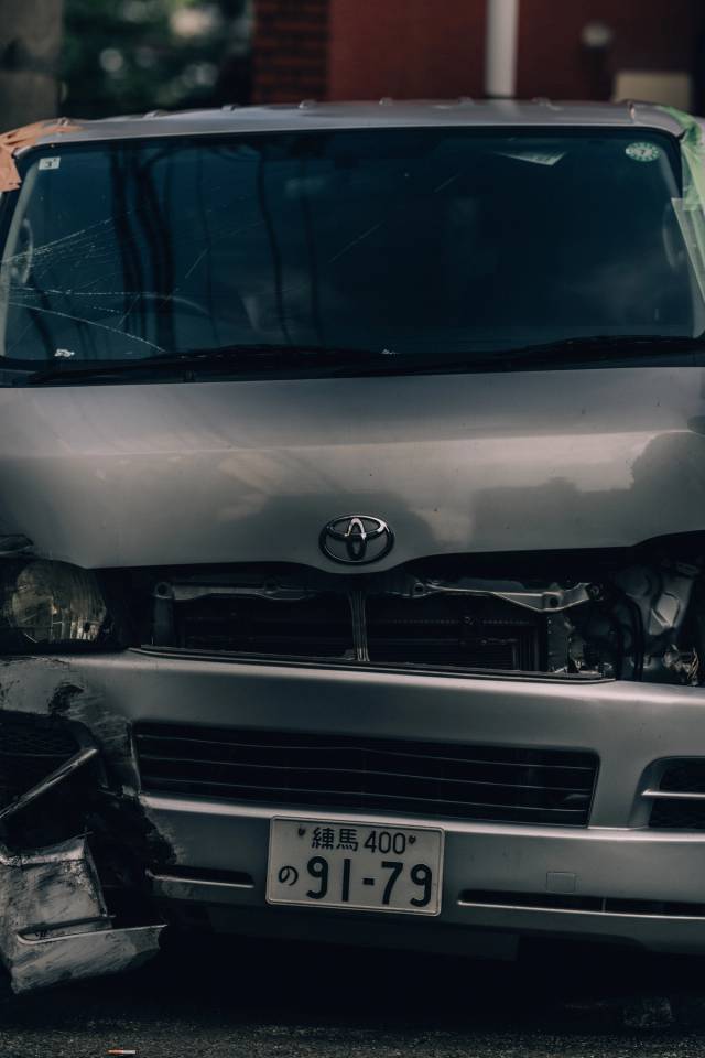 The front of a dented silver van with a cracked windshield and a Nerima license plate.
