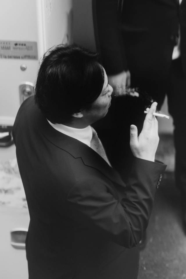 A suited man pausing to smoke, in black and white.