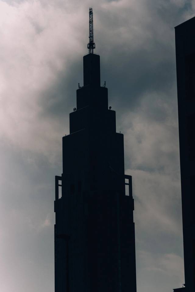 A tapering skyscraper in silhouette against a heavy overcast sky.