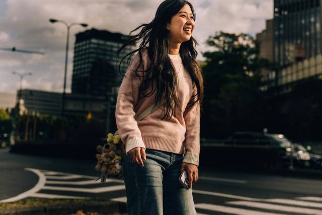 A woman laughs mid-stride on a city street, holding a phone and a bundle of small plush toys.