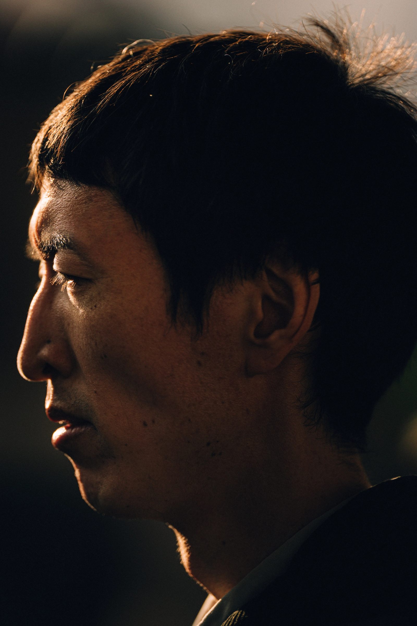 A man in profile, his face lit by a sliver of warm light against darkness.