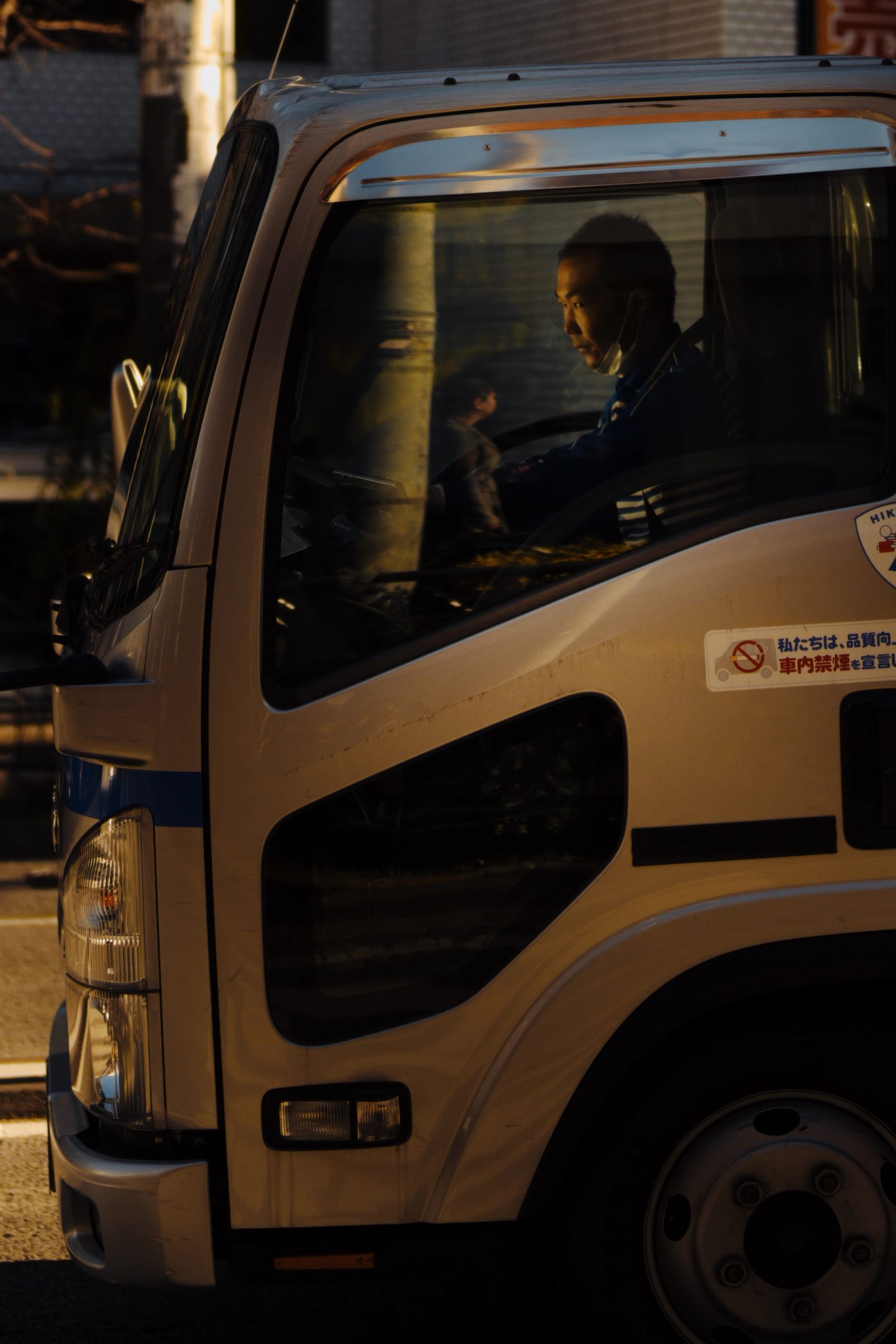 A delivery driver seen in profile through his cab window in warm evening light.