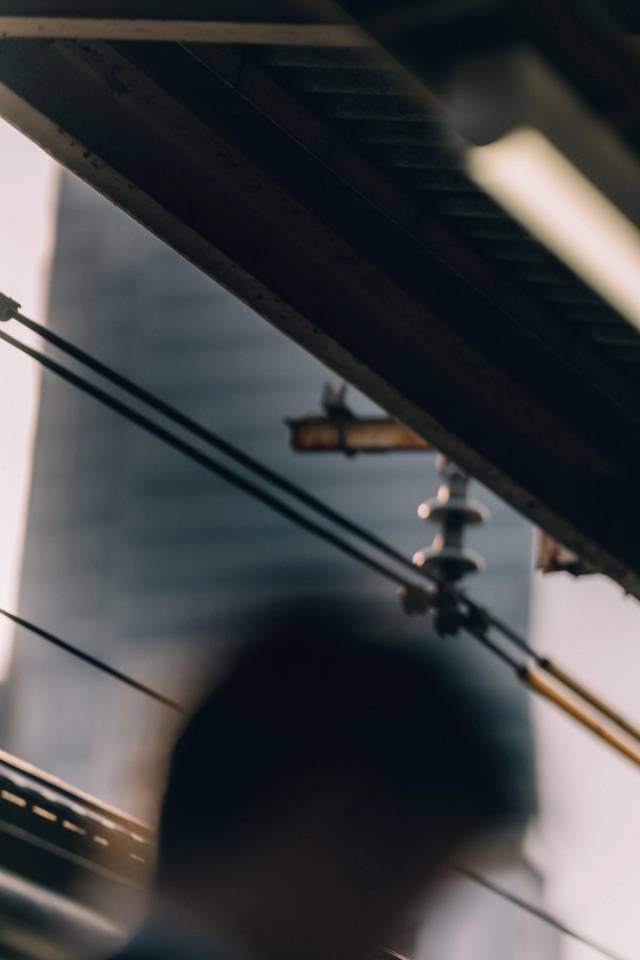 A view up into overhead train cables and a ceramic insulator, a silhouetted head blurred below.