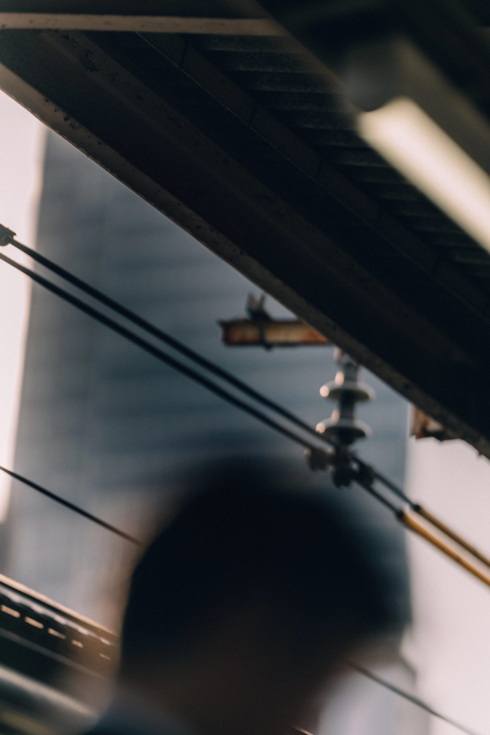 A view up into overhead train cables and a ceramic insulator, a silhouetted head blurred below.