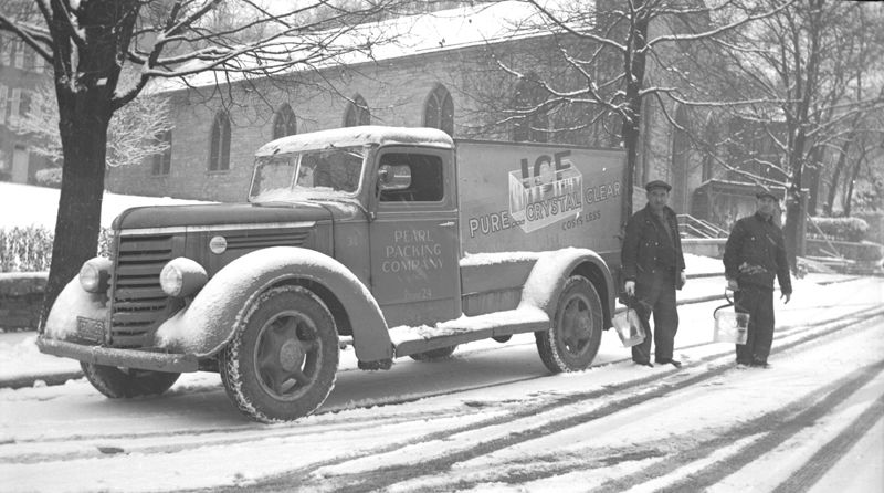 Ice truck in downtown Madison, Indiana with two men carrying blocks of ice.