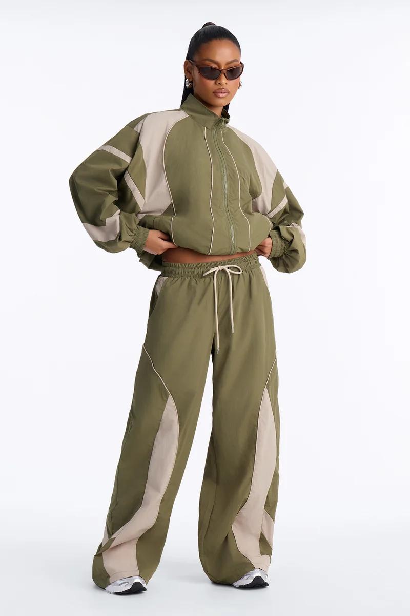 Model poses in a green and beige streetwear tracksuit with a zip-up windbreaker and wide-leg pants, showcasing a new sporty matching set.