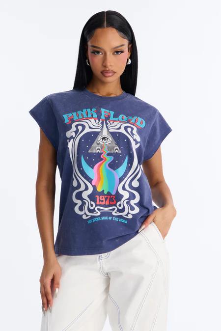 Woman in a navy blue Pink Floyd "Dark Side of the Moon" t-shirt featuring a pyramid, eye, and rainbow light, paired with white pants.