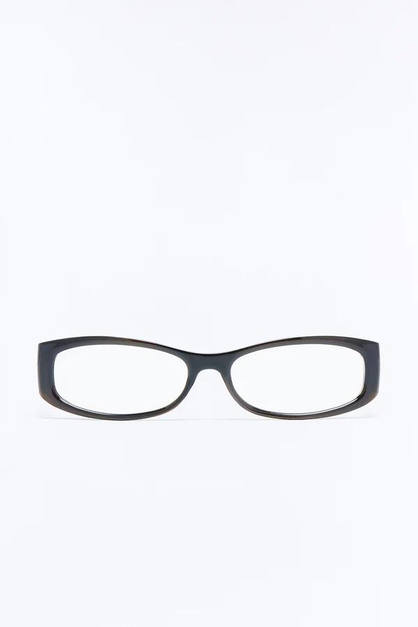 Elegantes gafas de montura gruesa y marrón oscuro, ligeramente rectangulares con lentes transparentes, centradas sobre un fondo blanco brillante.