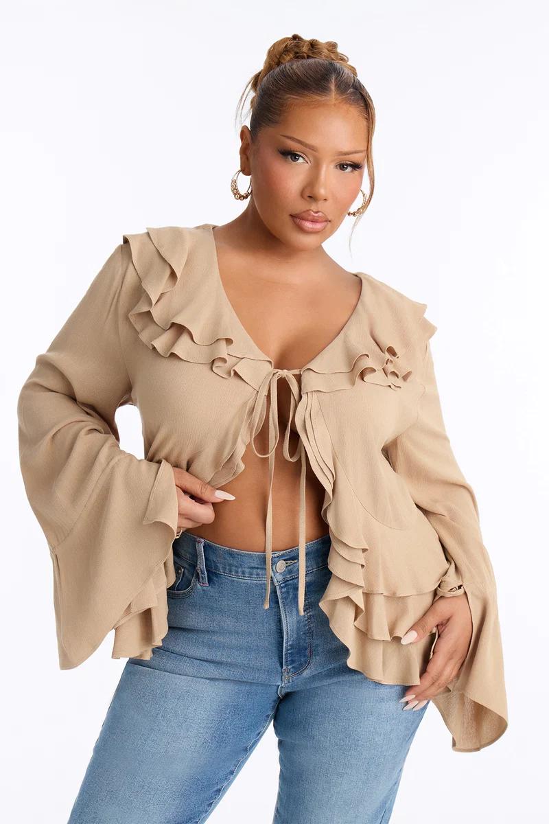 Model wearing a beige ruffled tie-front blouse with long bell sleeves and high-waisted blue jeans.