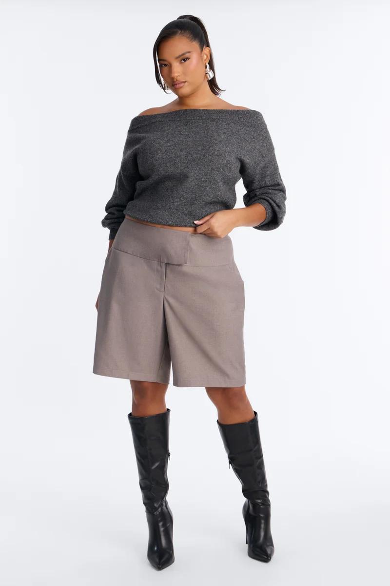 Model in a dark grey off-the-shoulder sweater, taupe tailored bermuda shorts, and black knee-high leather boots.