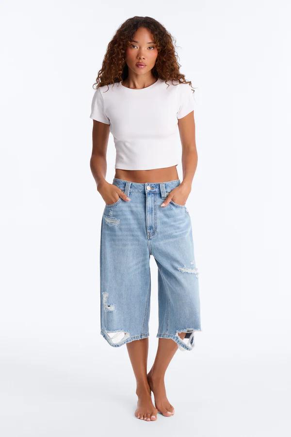 Mujer con pantalones culotte de mezclilla desgastada y camiseta corta blanca, modelando un estilo casual para la colección de moda.