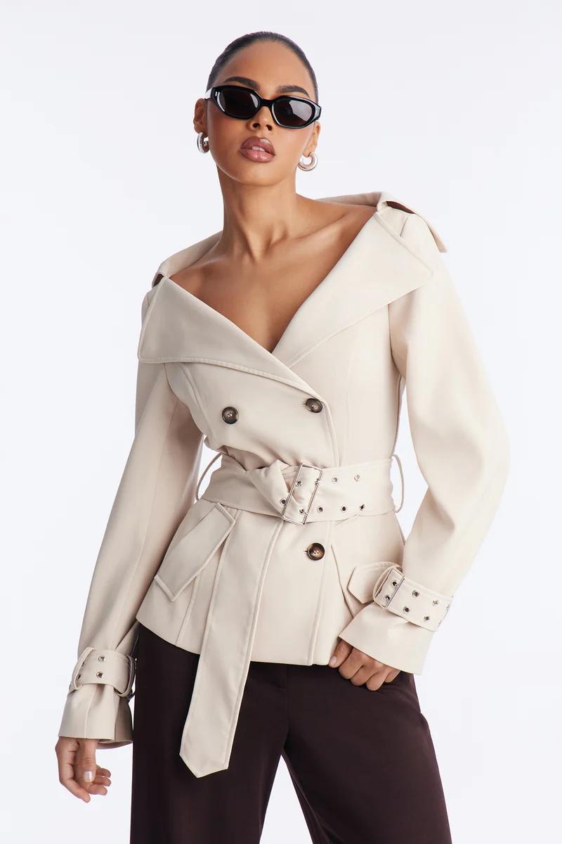Woman in a chic cream off-the-shoulder belted jacket with black sunglasses.