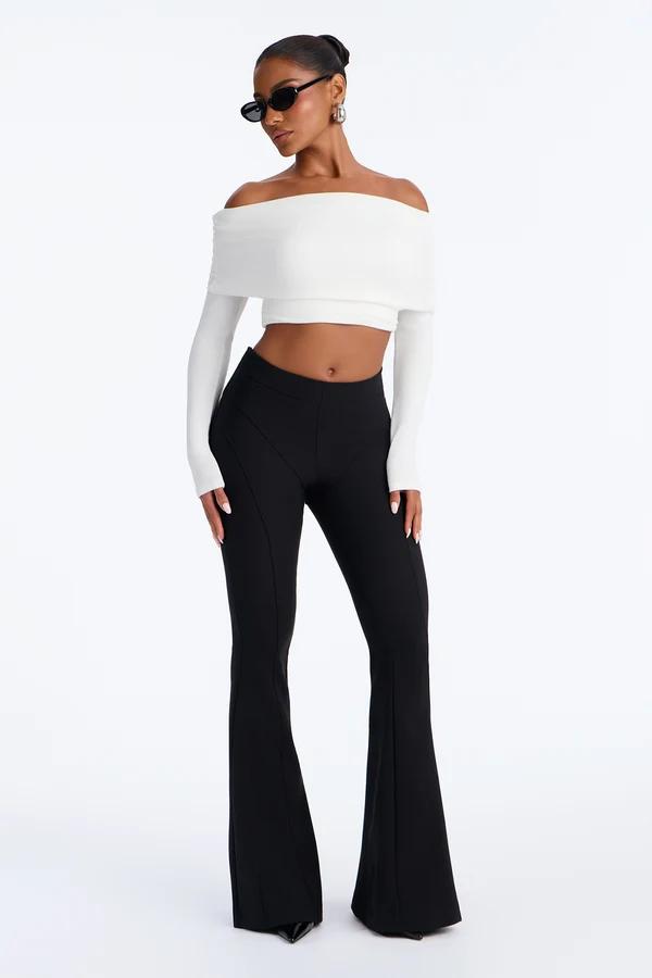 Modelo con top corto blanco de hombros descubiertos y pantalones acampanados negros de tiro alto, parte de una colección de moda moderna.