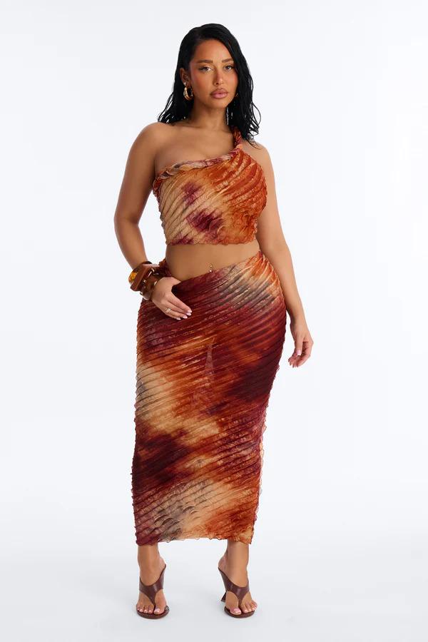 Woman wears a beige crochet strapless crop top with gold ring and a matching open-knit maxi skirt with ruffles.