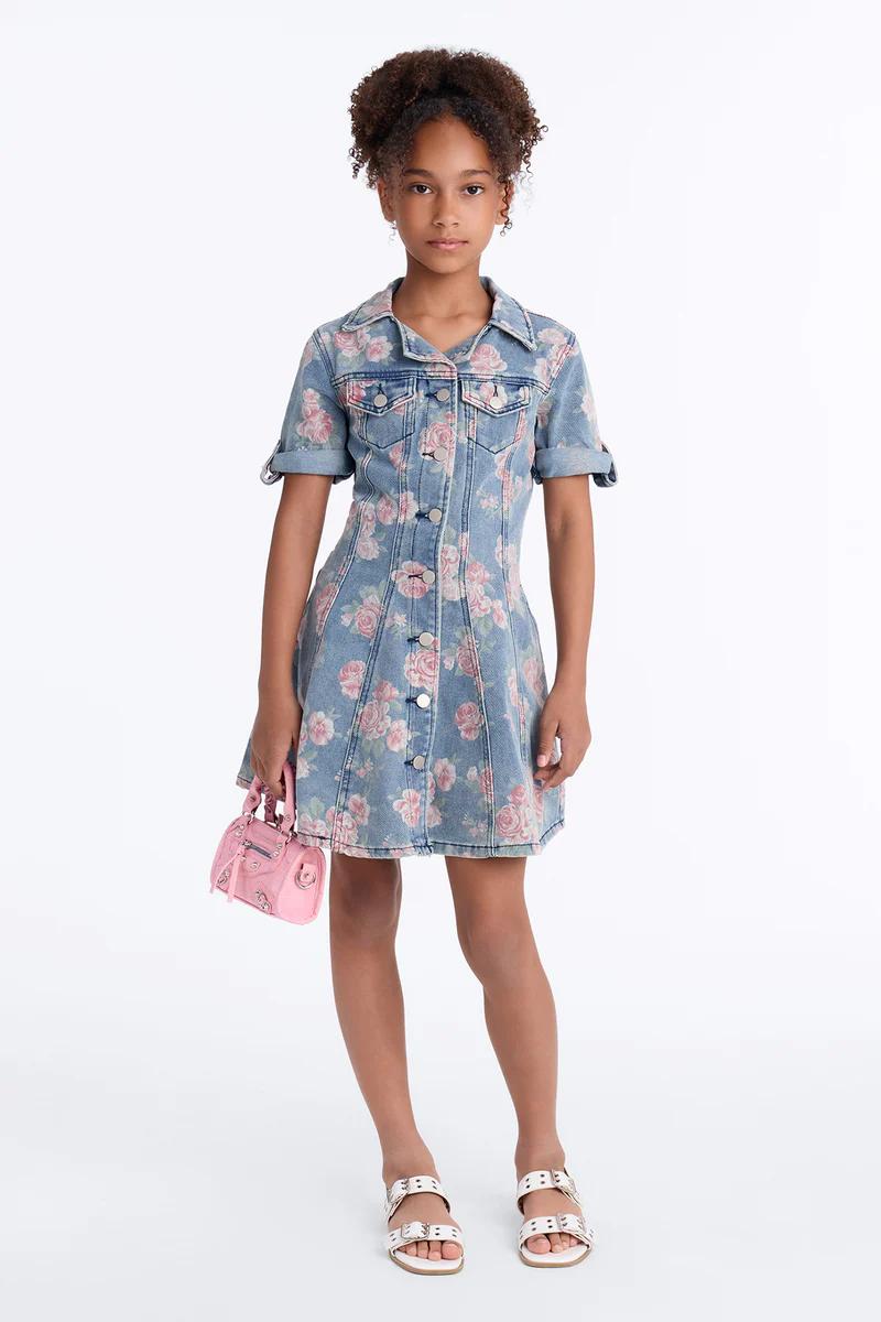 Niña con vestido vaquero azul claro de margaritas, gafas de sol cat-eye blancas y chanclas de corazón dorado. Vestido floral infantil.
