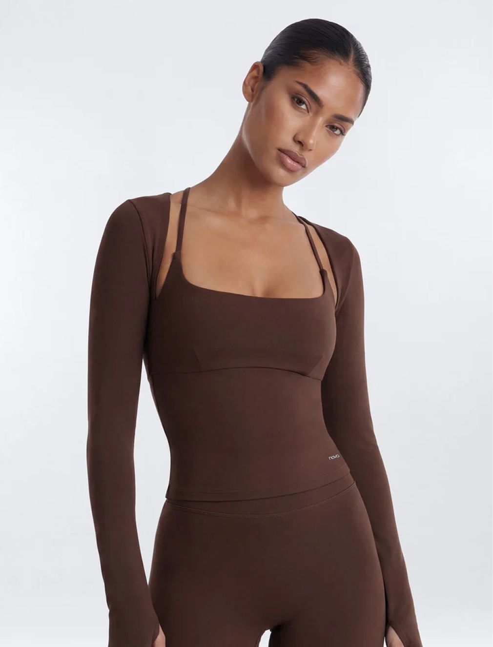 Model in a brown long-sleeve workout top and matching leggings from the new Novo athleisure collection against a white studio backdrop.