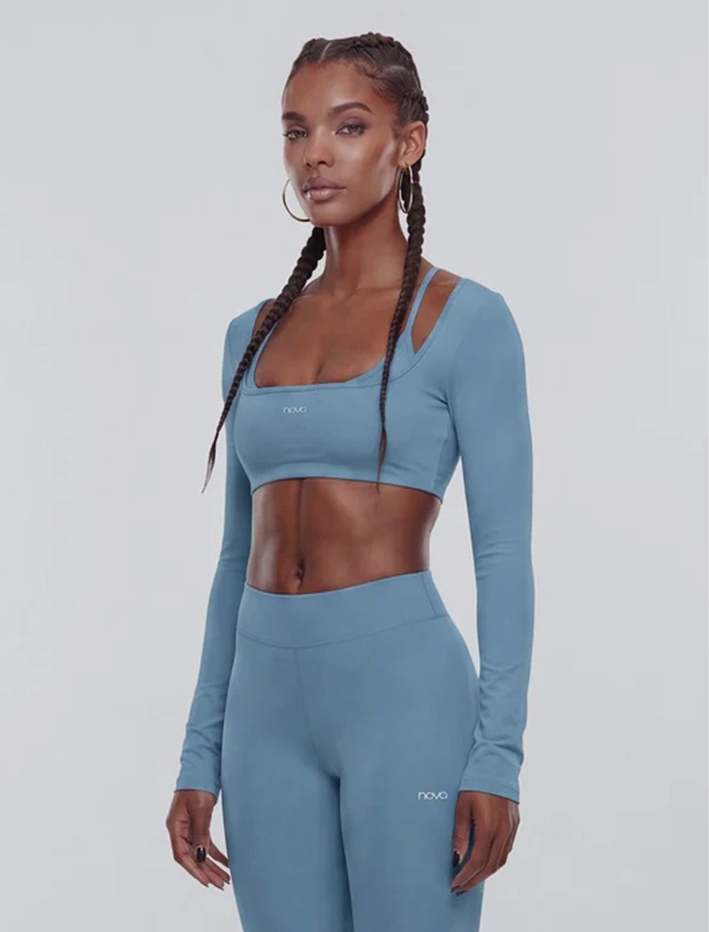 Woman wearing a dusty blue Nova activewear set featuring a long-sleeve crop top and matching leggings, showcasing modern gym apparel.