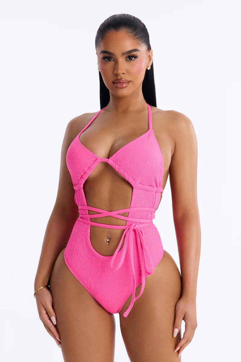 Stylish model in a vibrant hot pink textured cut-out monokini with wrap ties, showcasing modern swimwear trends for beach fashion.