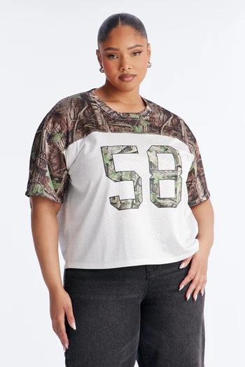 Plus-size woman wearing a white mesh football jersey with camouflage sleeves and a large camo number "58". She wears dark pants.