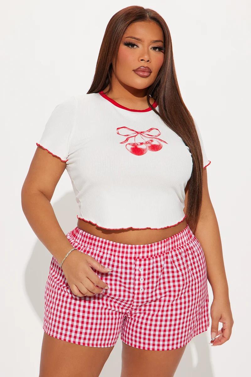 Plus size woman wearing a white cherry graphic crop top and red gingham pajama shorts.