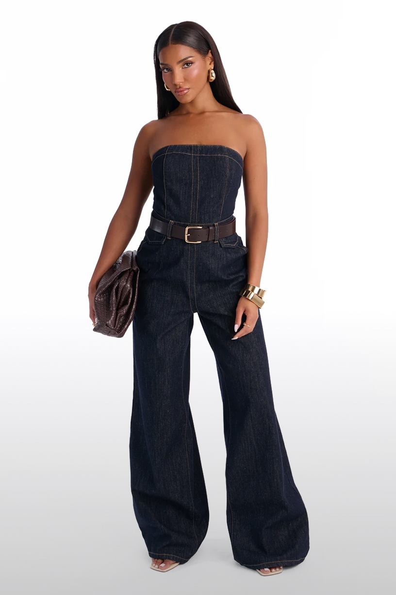 Woman modeling a strapless dark wash denim jumpsuit with a brown belt and wide-leg pants, showcasing a chic, trendy women's fashion look.