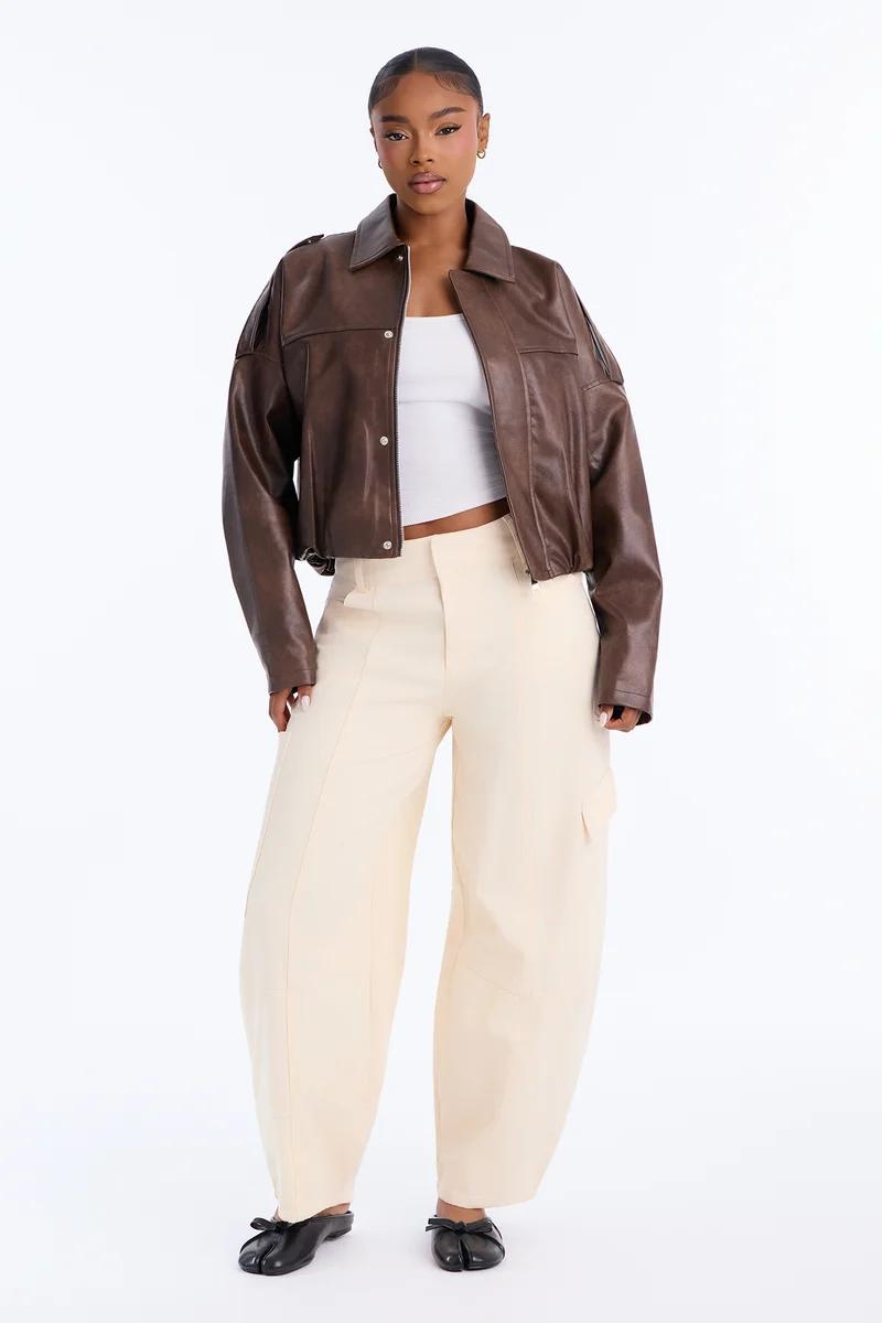 Woman wearing an oversized brown leather jacket, white crop top, cream wide-leg pants, and black Tabi flats.