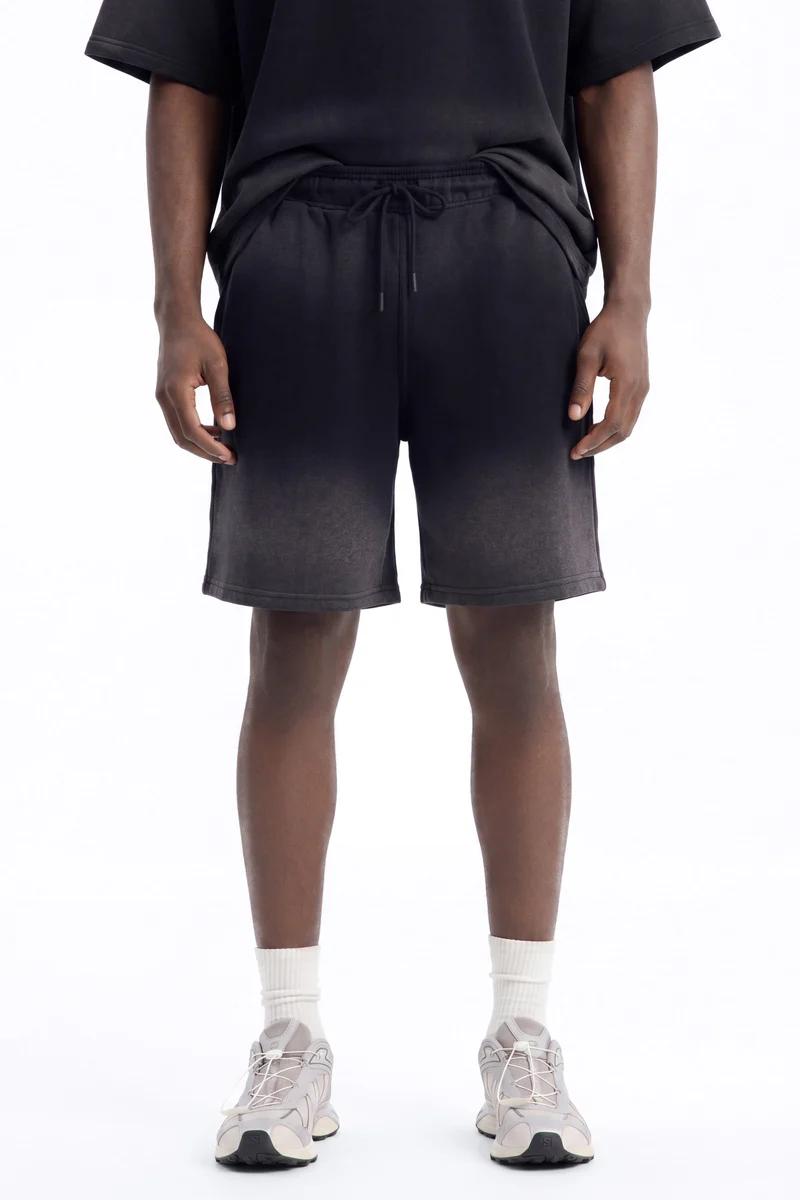 Man models black faded sweat shorts with a drawstring waist, perfect for casual or athletic wear. Showcasing comfortable men's fashion.