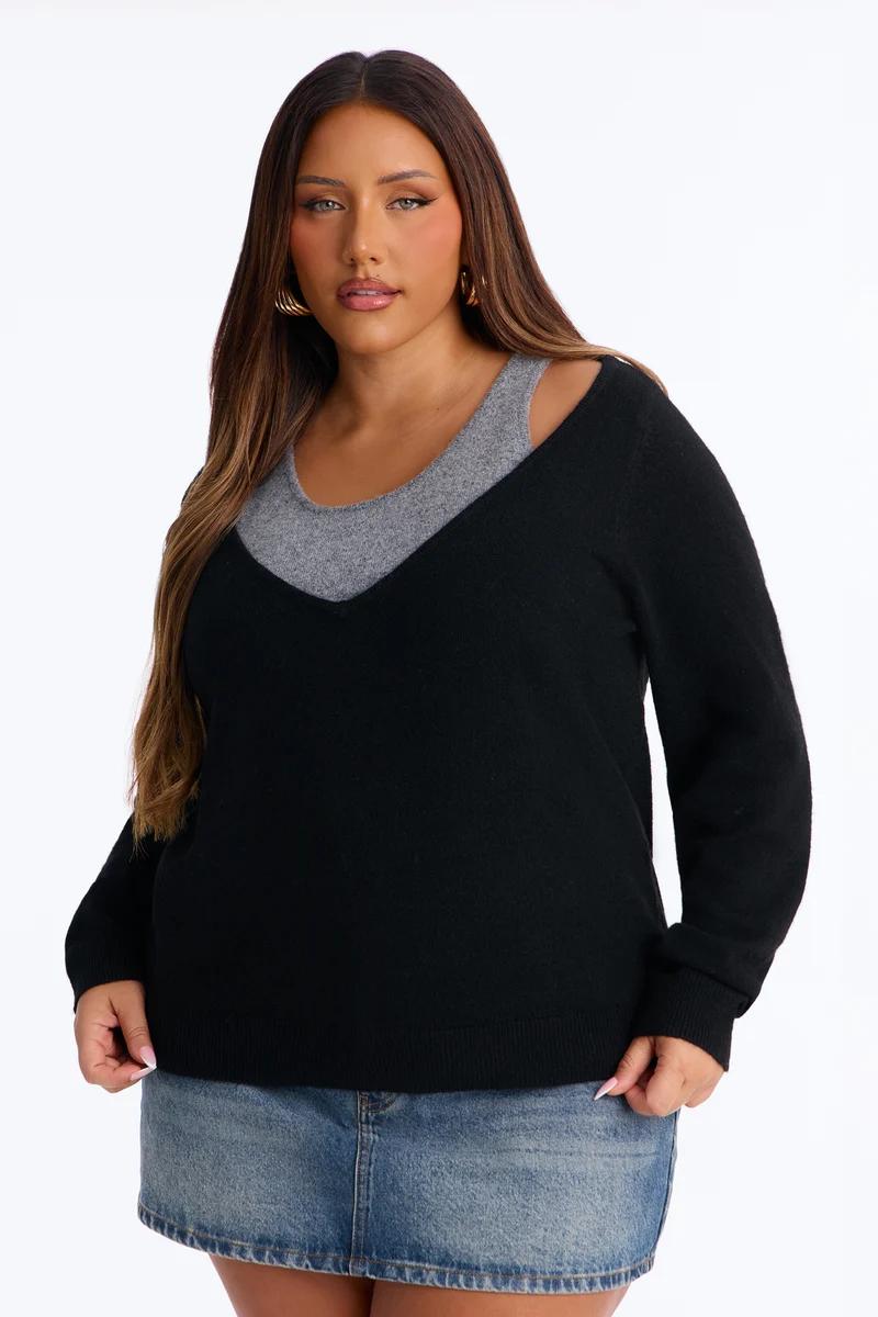 Plus size woman wearing a layered black v-neck sweater over a grey top and a denim miniskirt.