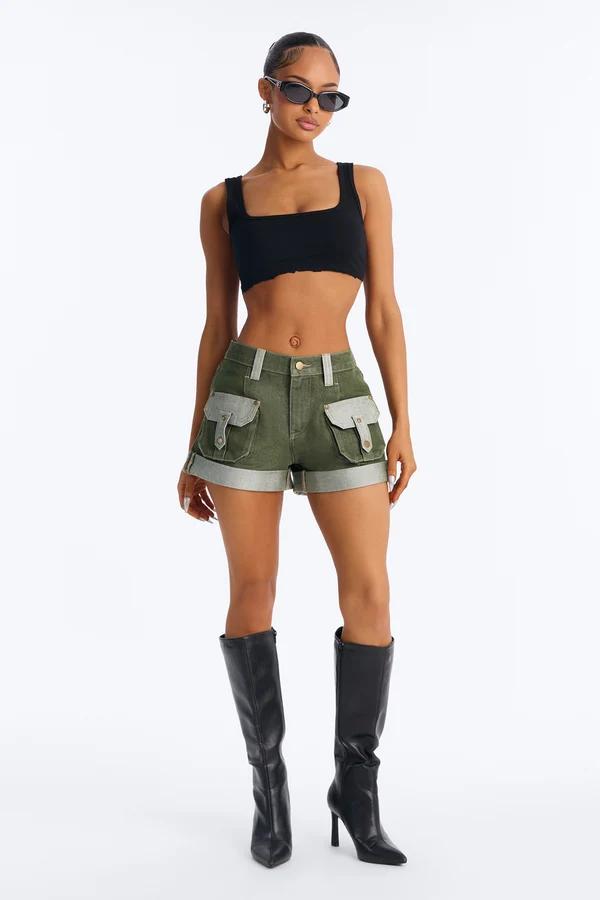 Model wears olive green cargo denim shorts, a black crop top, and knee-high leather boots for a trendy summer streetwear collection.
