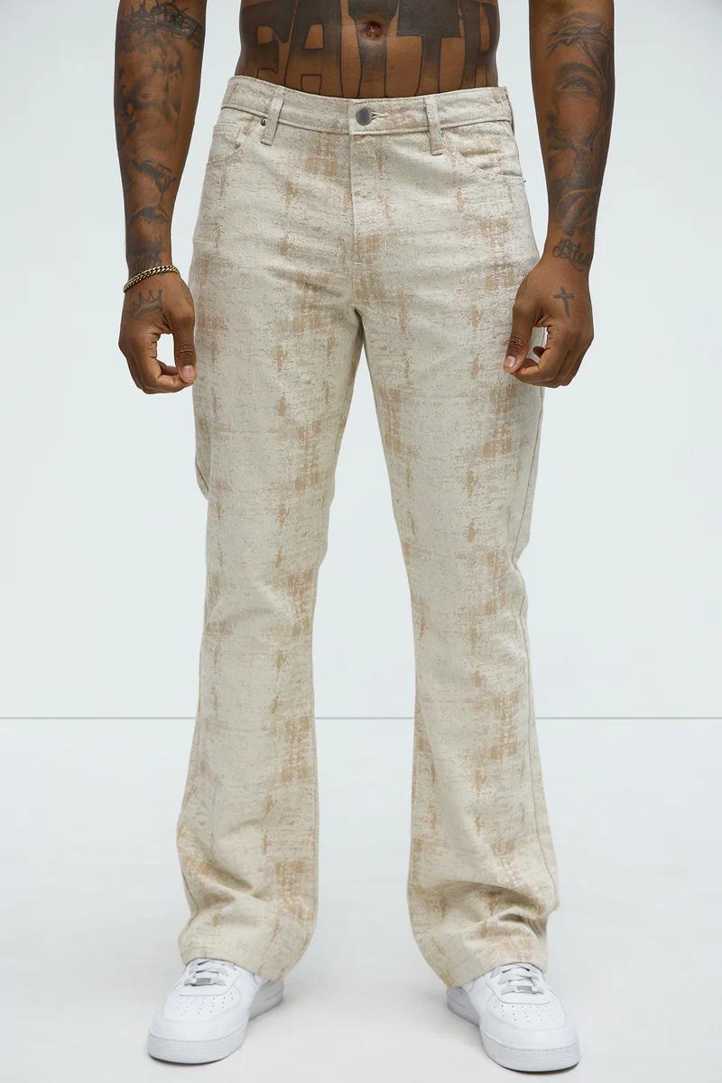 Hombre modelando nuevos pantalones acampanados beige con patrón bronceado desgastado y zapatillas blancas, destacando moda masculina.