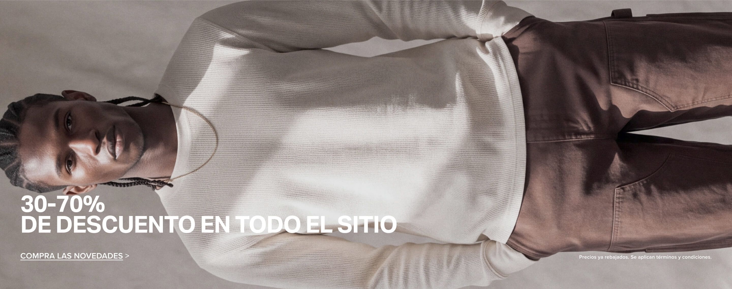 Hombre con camiseta de punto gofre color crema y pantalones marrones promueve una oferta del 30 al 70% de descuento en ropa nueva.