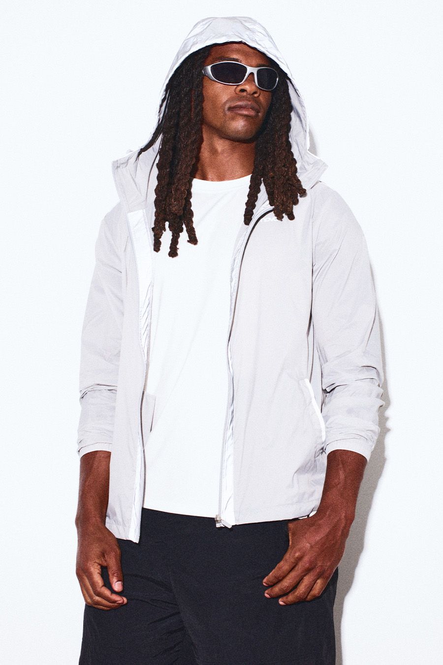 Man models light gray hooded athletic jacket, white tee, black shorts, silver sunglasses. Promotes men's activewear collection.