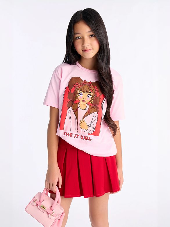 Stylish girl in a pink "THE IT GIRL" graphic t-shirt, a red pleated skirt, and a matching pink mini handbag, showcasing a trendy kids' outfit.