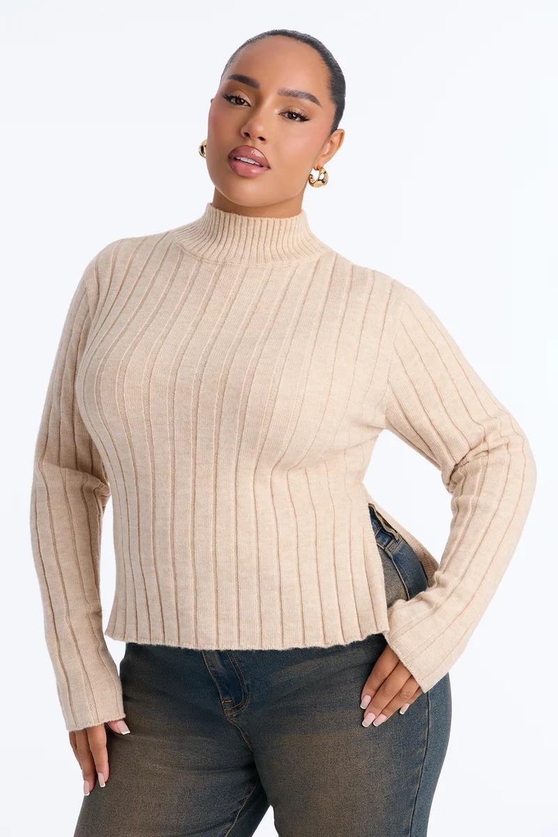 Plus-size woman wearing a beige ribbed mock-neck sweater with side slits and dark jeans.