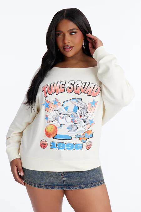 Woman in a cream 'Tune Squad' sweatshirt with Bugs Bunny playing basketball and a denim mini-skirt, posing confidently.