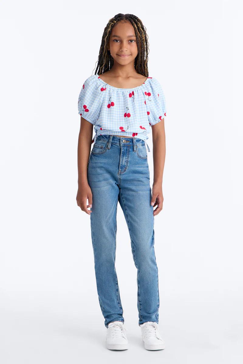 Smiling girl in a blue gingham cherry crop top, high-waisted jeans, and white sneakers. Trendy youth fashion.