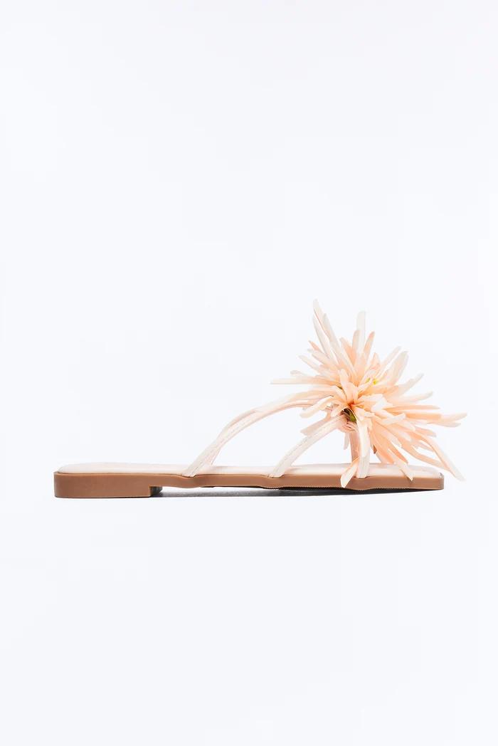 Sandalias planas color melocotón con una gran flor decorativa.