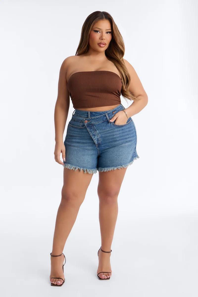 Plus size woman in a brown strapless tube top and criss-cross waist denim shorts.