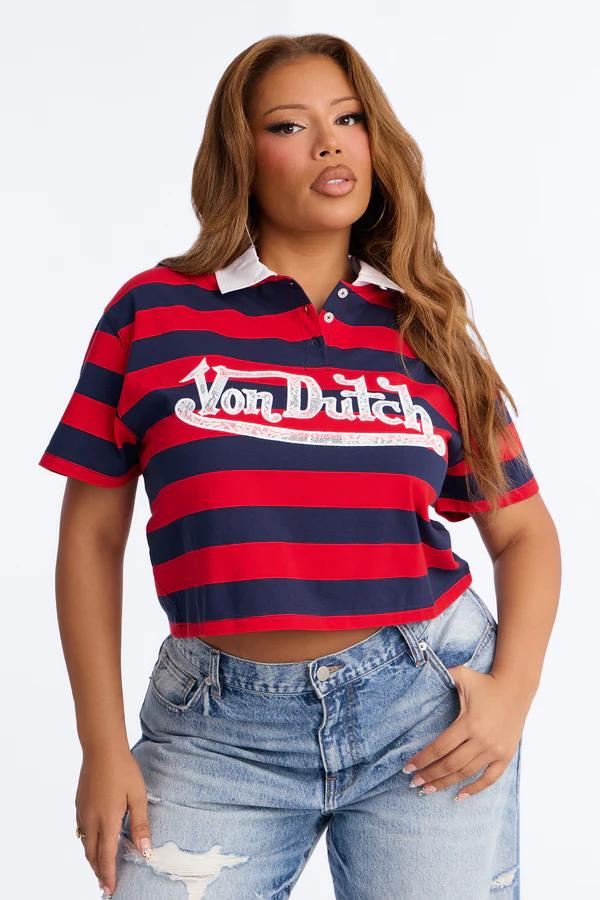 Woman wearing a red and navy striped cropped Von Dutch polo shirt with a white collar and light wash distressed jeans, posing.