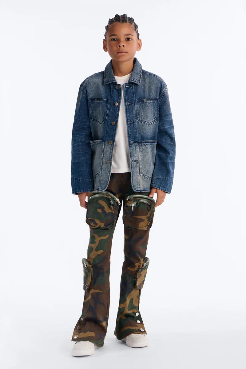 Joven modela chaqueta vaquera azul desgastada y pantalones cargo camuflaje, parte de nueva colección streetwear infantil.