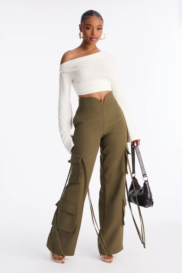Una mujer modela un top corto crema sin hombros y pantalones cargo verde oliva con bolsillos y lazos, sosteniendo un bolso negro.