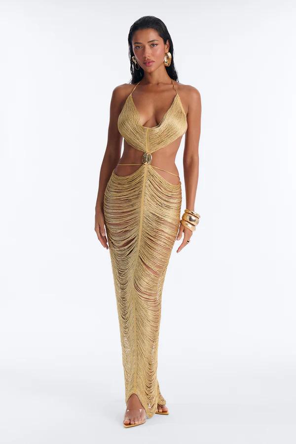 Woman posing in a two-piece brown and cream striped knit outfit with tiered fringe, a waist cutout, gold arm cuff, and braided clutch bag.