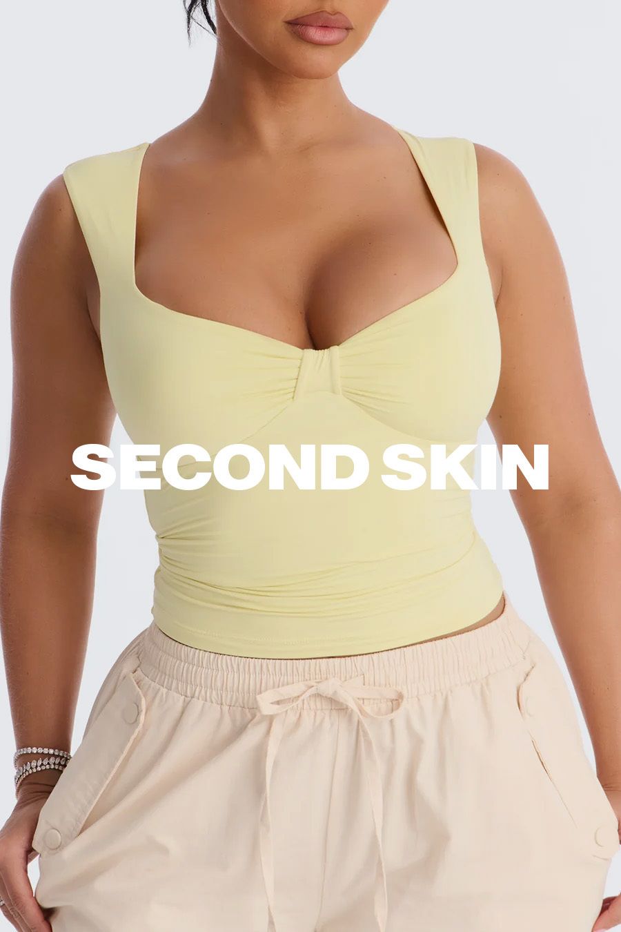 Mujer en top amarillo pálido "SECOND SKIN" y pantalón beige con cordón, promocionando ropa cómoda y de ajuste perfecto.