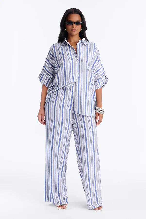 Stylish woman in a pink striped strapless plus size jumpsuit, featuring wide-leg pants and a drawstring waist, perfect for summer fashion.