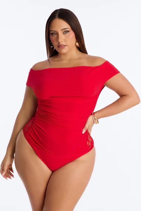 Confident woman in a red off-shoulder ruched bodysuit with side lace details, wearing gold earrings and bracelets.