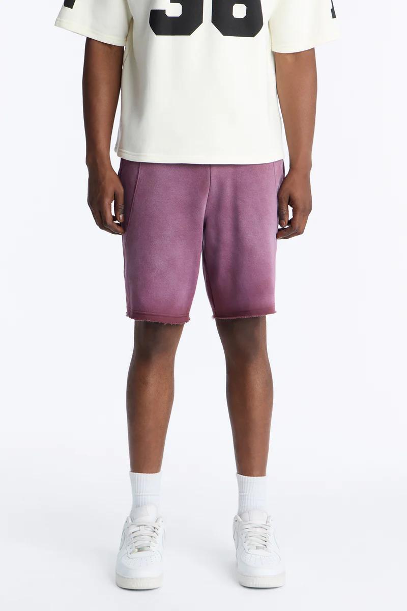 Person in cream tee & faded purple casual shorts with raw hem, white socks, and white sneakers, showcasing summer streetwear.