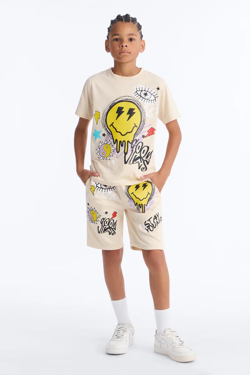 Joven viste camiseta gráfica beige y shorts a juego con diseño de rayo y cara sonriente. Atuendo juvenil casual, perfecto para el buen rollo.